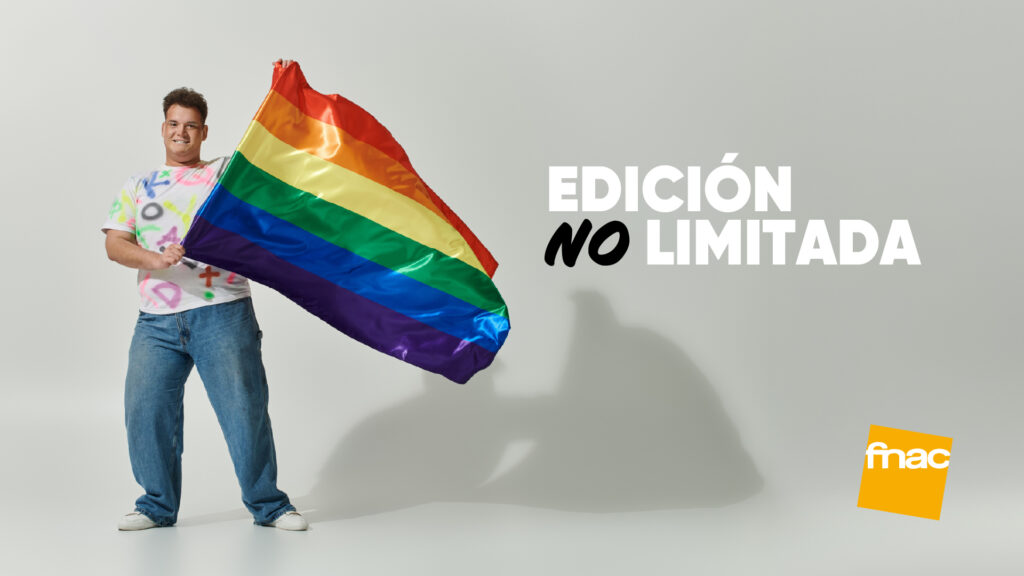 Chico con vaqueros y camiseta pintada sosteniendo una gran bandera del Orgullo sobre un fondo gris claro con el logotipo de Fnac
